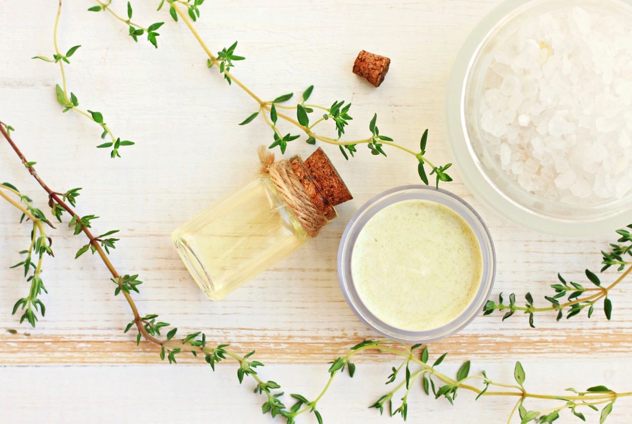 A jar of lotion next to some herbs.