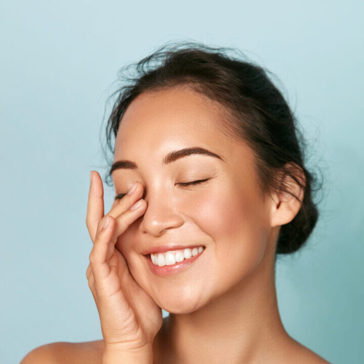 Beauty face. Smiling asian woman touching healthy skin portrait. A woman with her eyes closed touching her face.
