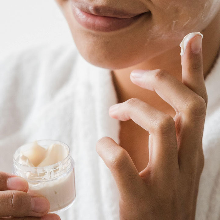 A woman is putting cream on her face