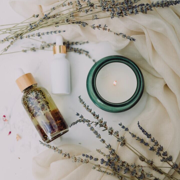 A bottle of lotion, candle and lavender flowers.